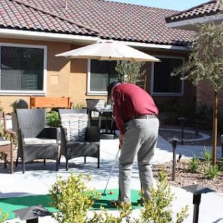 A person playing golf on a putting green in a garden setting.