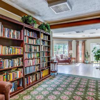 A cozy library corner with a large bookshelf filled with books, comfortable seating, and natural light streaming through the windows.