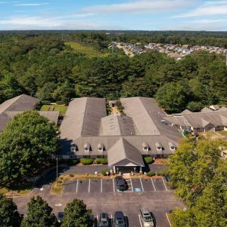Aerial view of a building surrounded by trees with a parking lot in the foreground.