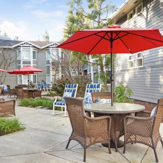 A cozy residential patio area with wicker furniture and red umbrellas for shade.