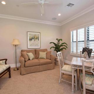 A cozy living room featuring a sofa, dining table with chairs, a tall lamp, and an indoor plant near the window.