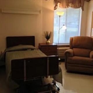 A cozy hospital room with a bed, recliner chair, and a standing lamp by the window.