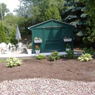A landscaped garden with a green shed, patio seating, and various plants.