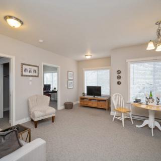 A cozy living room with neutral tones, featuring comfortable furniture and a small dining area by the window.