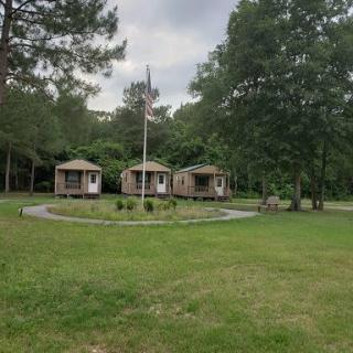 Three small cabins surrounded by trees and grass under an overcast sky.
