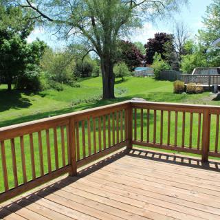 A sunny backyard view from a wooden deck, featuring lush green grass and trees.