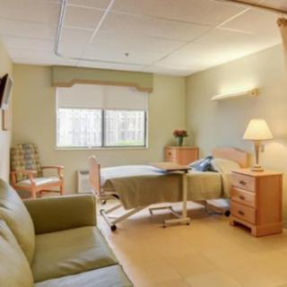 A well-lit hospital room with a bed, side table, chair, and lamp.