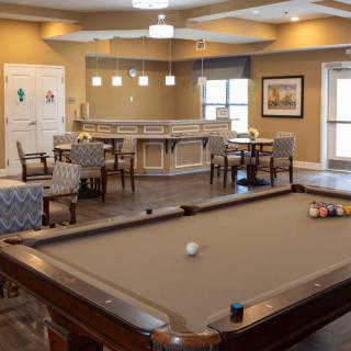 A cozy game room featuring a pool table, seating area, and bar counter.