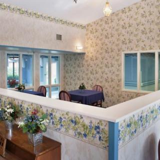 A cozy dining area with floral wallpaper, featuring tables and chairs beside large windows.