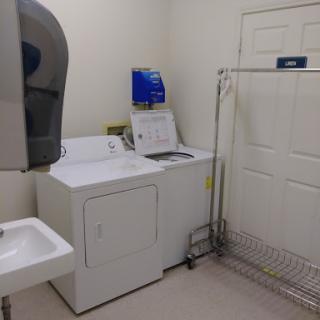 A clean and organized laundry room featuring a washing machine, dryer, sink, and clothes rack.