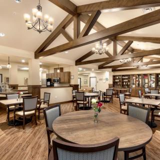 A warmly lit dining area with wooden beams, chandeliers, and neatly arranged tables and chairs.
