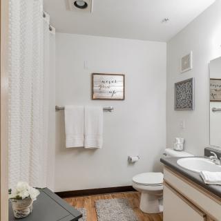 A clean and simple bathroom with white walls, featuring a sink, mirror, toilet, and neatly hung towels.
