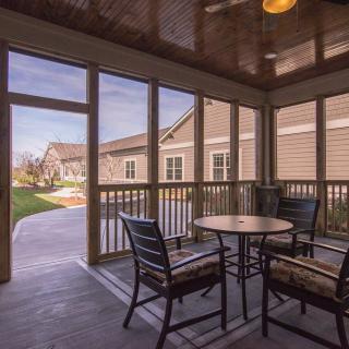 A cozy screened porch with outdoor furniture, featuring a table and chairs, overlooks a residential area.