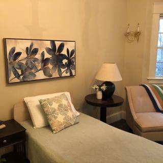 A cozy bedroom with a single bed, wall art, and a comfortable chair.