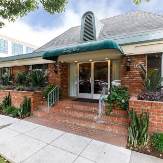 A charming brick building with a green awning, featuring a welcoming entrance adorned with plants.