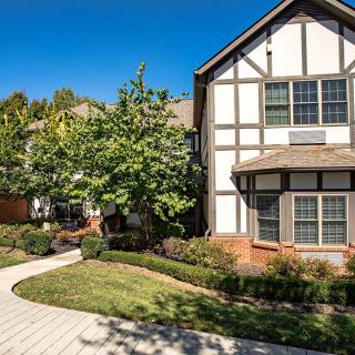 A charming residential house with a mix of brick and wood architecture, surrounded by a well-maintained garden and a paved pathway.