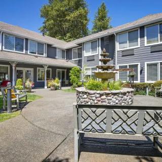 A sunny courtyard with a central fountain surrounded by a two-story building and outdoor seating.