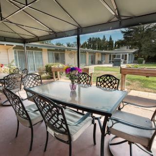 A cozy outdoor dining area with a table and chairs under a canopy, surrounded by greenery.