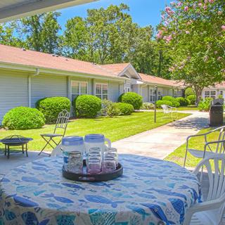 A sunny outdoor patio with a table and chairs, overlooking a well-maintained garden.