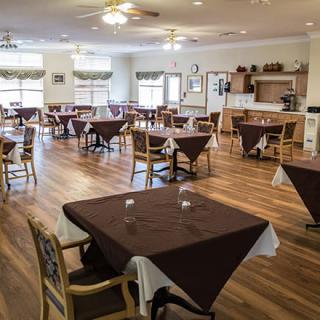 An empty dining room with neatly arranged tables and chairs, featuring a wooden floor.