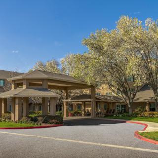 A sunny view of a building entrance surrounded by trees and landscaped grounds.