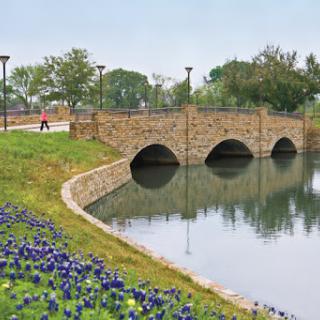 A serene view of a stone bridge arching over calm waters, surrounded by colorful flowers and greenery.