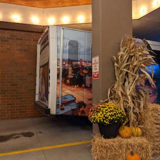 A truck partially parked near autumn decorations, featuring pumpkins and hay.