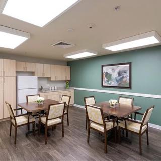 A modern dining area with tables, chairs, and a small kitchen setup featuring a green accent wall and framed artwork.