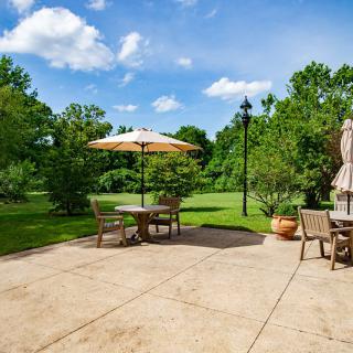 A sunny patio with outdoor furniture and an umbrella overlooking a lush garden.