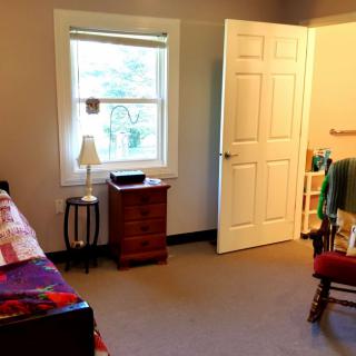 A cozy bedroom with a bed, nightstand, and a window letting in natural light.