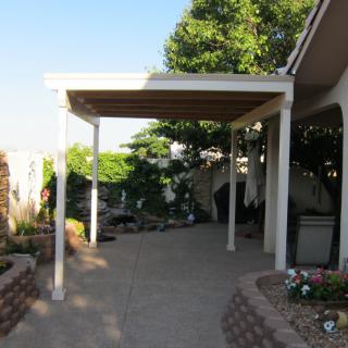A backyard patio with an awning providing shade over a paved area, surrounded by greenery.