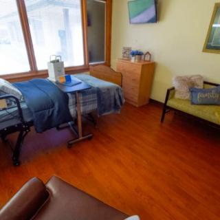A cozy bedroom with a single bed, wooden flooring, and a comfortable chair next to large windows.