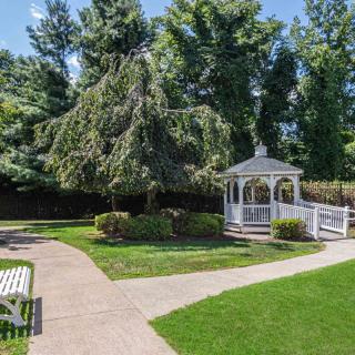 A serene garden with a white gazebo, surrounded by lush greenery and trees.