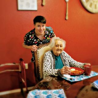 A family member posing with an elderly woman at the dining table.