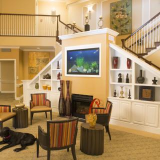 A modern living room with a cozy seating area, featuring an aquarium above the fireplace and a staircase leading to the upper level.