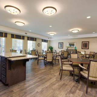 A spacious dining area with multiple tables and chairs, featuring wooden floors and ceiling lights.