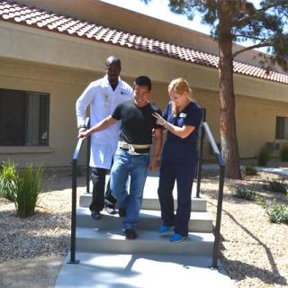 Medical professionals assist a patient with walking exercises outdoors.