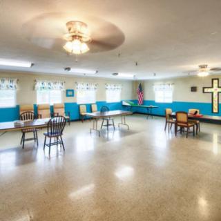 A spacious room with chairs, tables, and a cross on the wall.