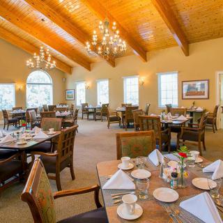 An elegant dining room with wooden ceilings, chandeliers, and neatly set tables.