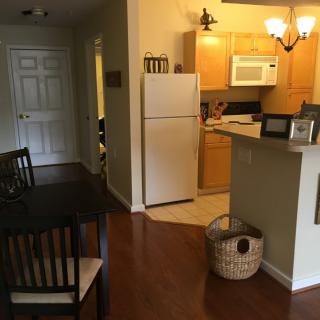 A cozy apartment kitchen with wooden flooring, featuring a dining table, refrigerator, and microwave.