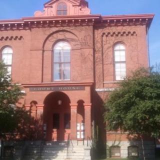 Historic brick building with arched windows and trees on a sunny day.