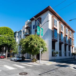 A modern apartment building on a sunny street corner with trees nearby.