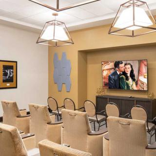 A cozy theater room with beige seating and a large TV screen, featuring elegant lighting and wall art.