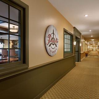 A well-lit hallway with carpeted flooring and windows, featuring a sign on the wall.