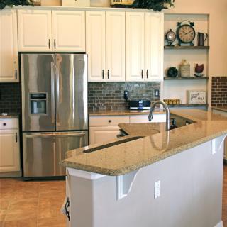 A modern kitchen with a stainless steel refrigerator, white cabinets, and a granite countertop island.