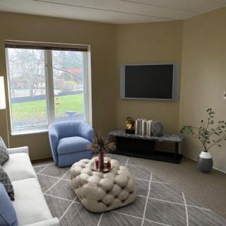 A cozy living room with modern decor, featuring a sofa, armchair, tufted ottoman, and a wall-mounted television.