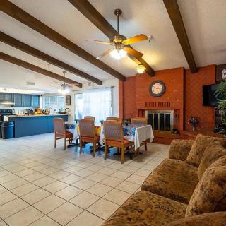 A cozy living room with an open floor plan, featuring a dining area, kitchen, and fireplace under a beamed ceiling.