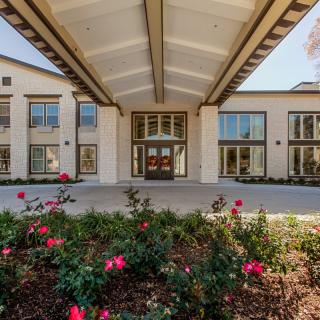 The image shows the front entrance of a modern building with landscaping and vibrant flowers.