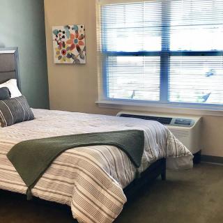 A cozy bedroom with a neatly made bed, decorative pillows, and light streaming through a window.