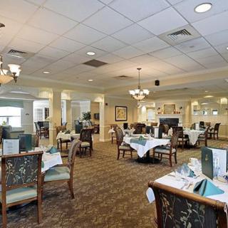 An elegant restaurant dining area with neatly arranged tables and chairs, featuring chandeliers and a carpeted floor.